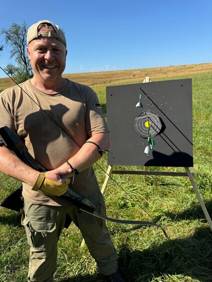 A person in a field holding a bow, standing next to a target with arrows. 1