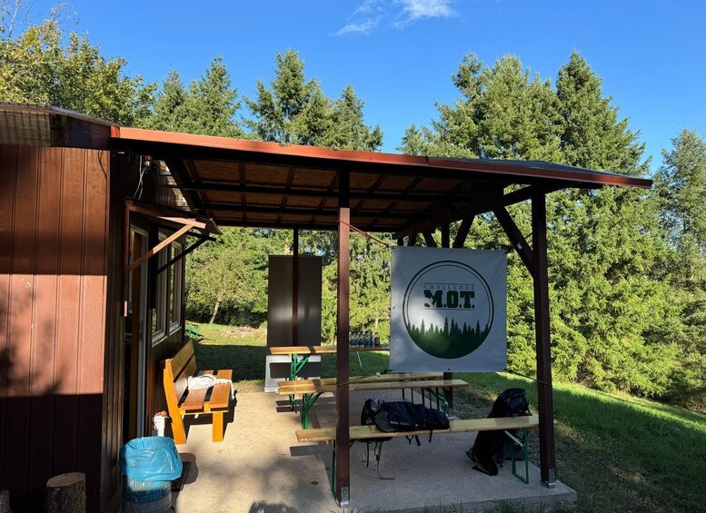A wooden cabin with a covered outdoor area, picnic tables, and a sign reading 'CHALLENGE M.O.T.' 3
