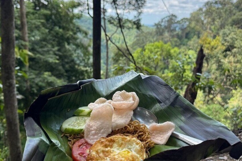 A meal served on a banana leaf with noodles, a fried egg, and vegetables in a forest setting. 2