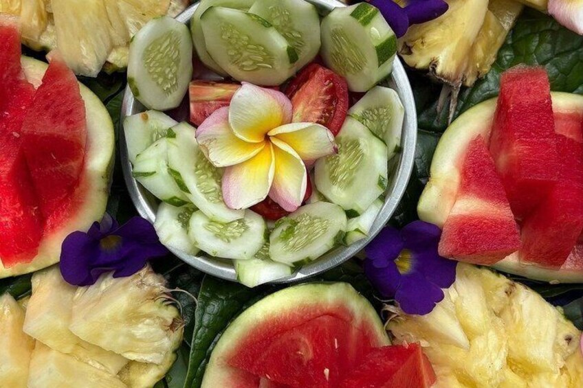 A fruit salad with watermelon, pineapple, and cucumber slices, surrounded by purple flowers. 4