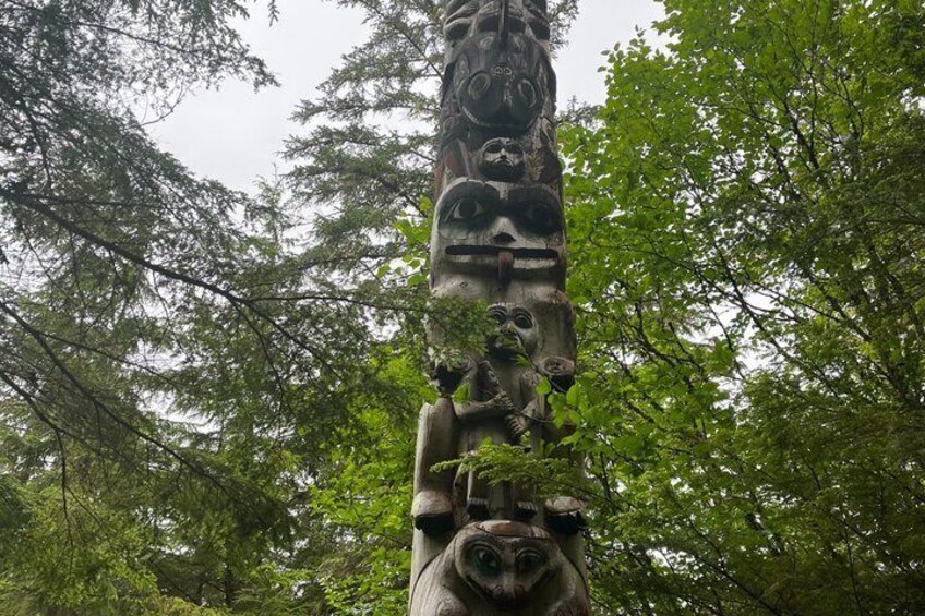 En totempæl med flere figurer, omgivet af tæt skov. 4