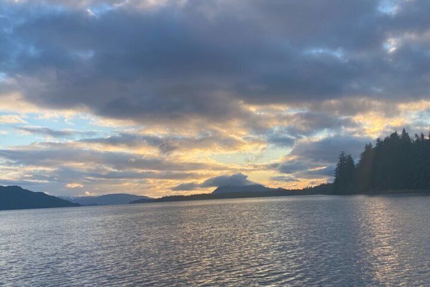 A calm lake with a forested shoreline and distant mountains under a cloudy sky. 4