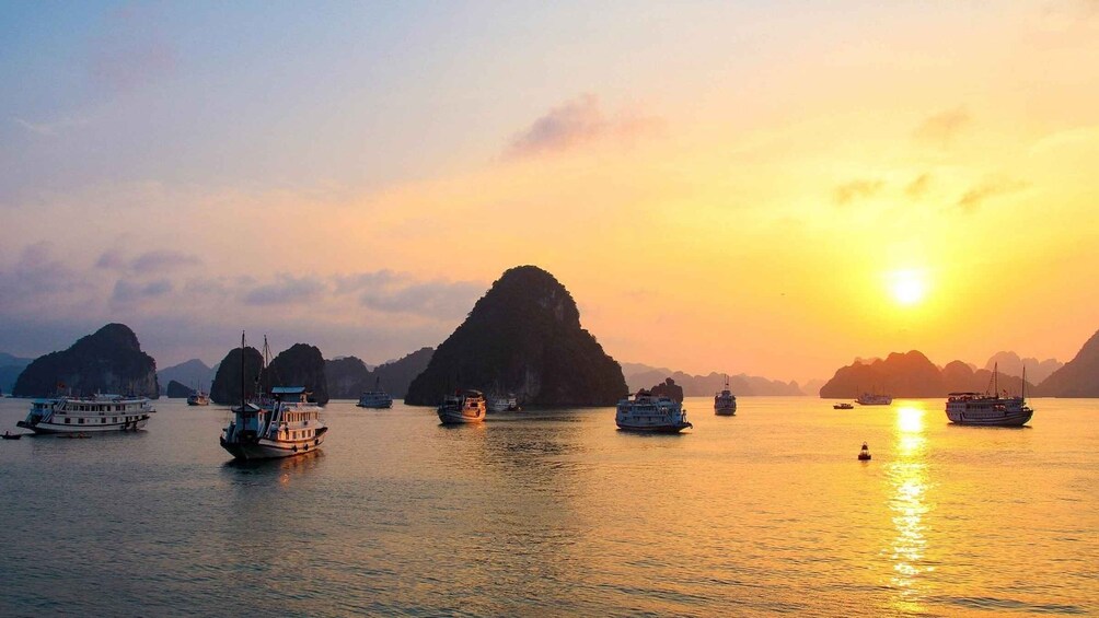 Un atardecer sobre un cuerpo de agua con varias embarcaciones y islas de piedra caliza. 1