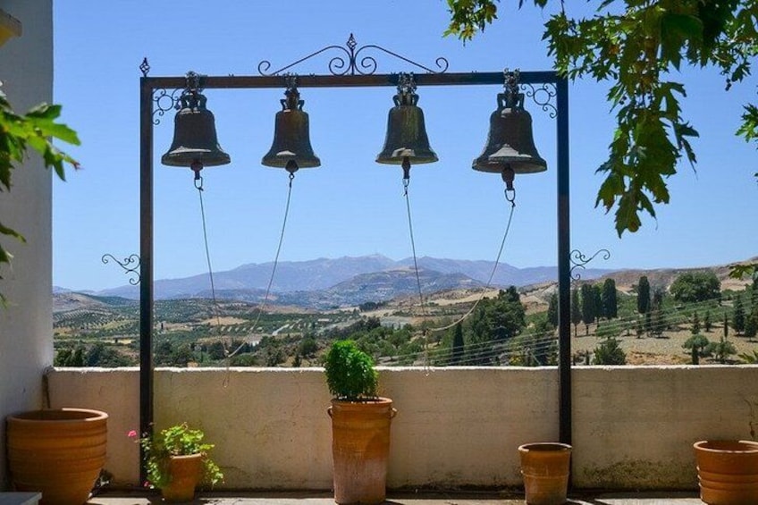 A balcony with terracotta pots and a metal bell structure against a mountainous backdrop. 2