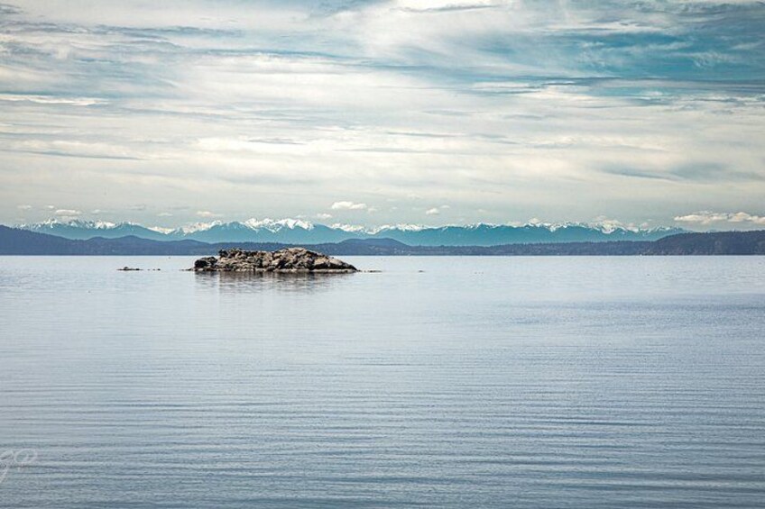 Un lago tranquilo con una pequeña isla en el centro y montañas nevadas al fondo. 3