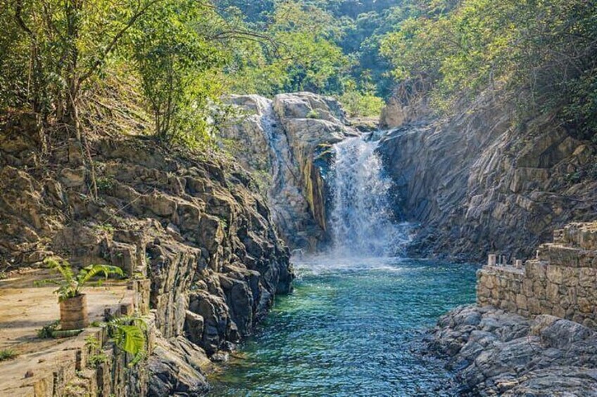 A waterfall cascading into a river surrounded by rocky cliffs and dense greenery. 1