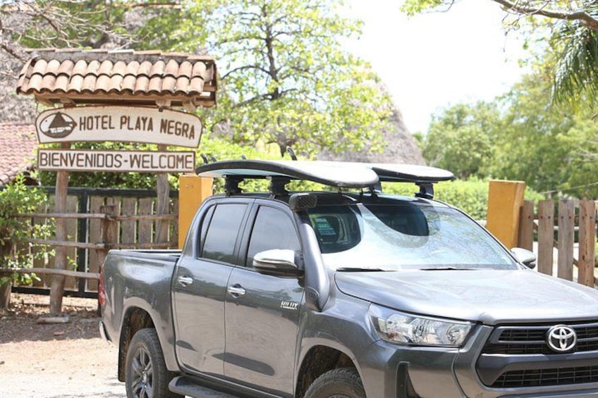 En grå Toyota pickup lastbil parkeret foran en træport med et skilt, der viser 'Hotel Playa Negra' og 'Bienvenidos-Welcome'. 1