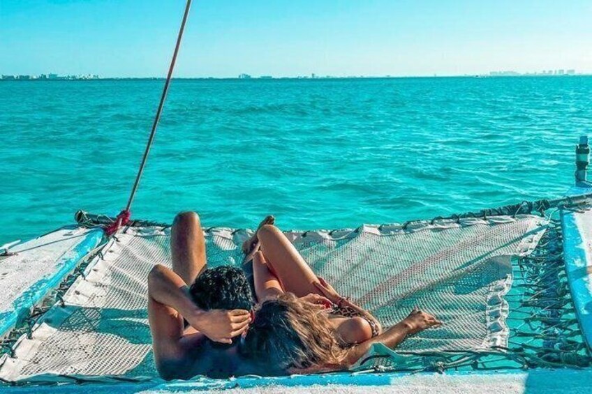 A person lying on a hammock on a boat with turquoise water in the background. 1