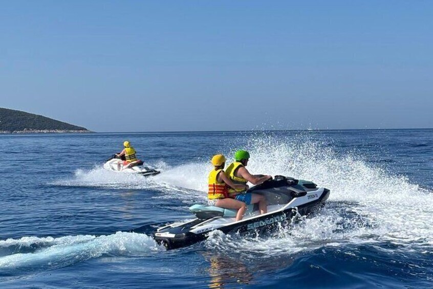 Two people jet-skiing on a clear blue sea with a distant landmass. 3