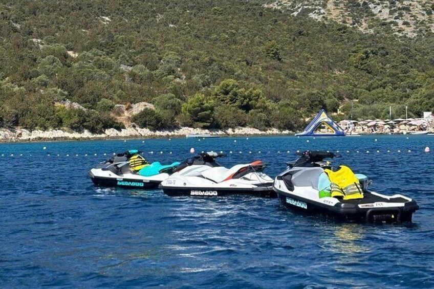 Two Sea-Doo jet skis on a calm body of water with a rocky shoreline and a small inflatable structure in the background. 4