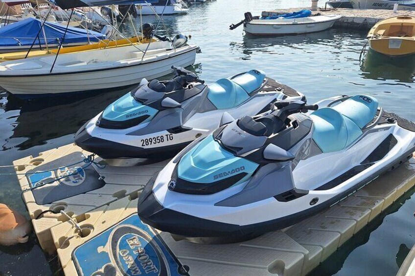 Two Sea-Doo jet skis docked at a marina with other boats in the background. 5