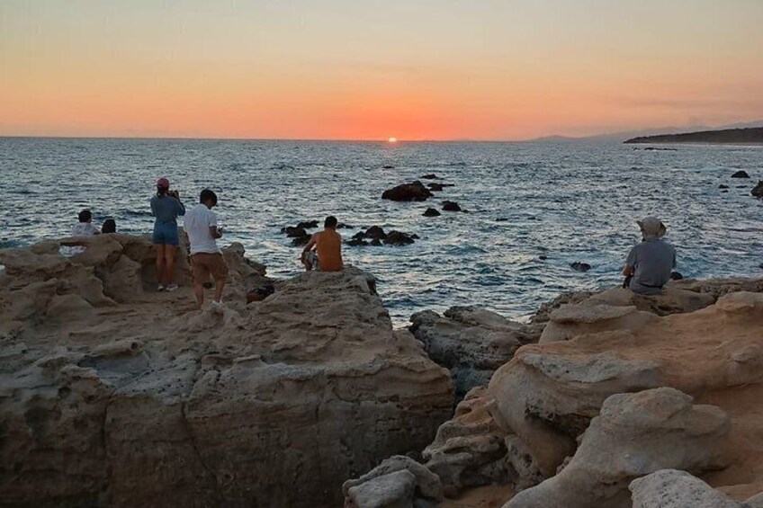 People sitting on rocks by the sea at sunset. 4