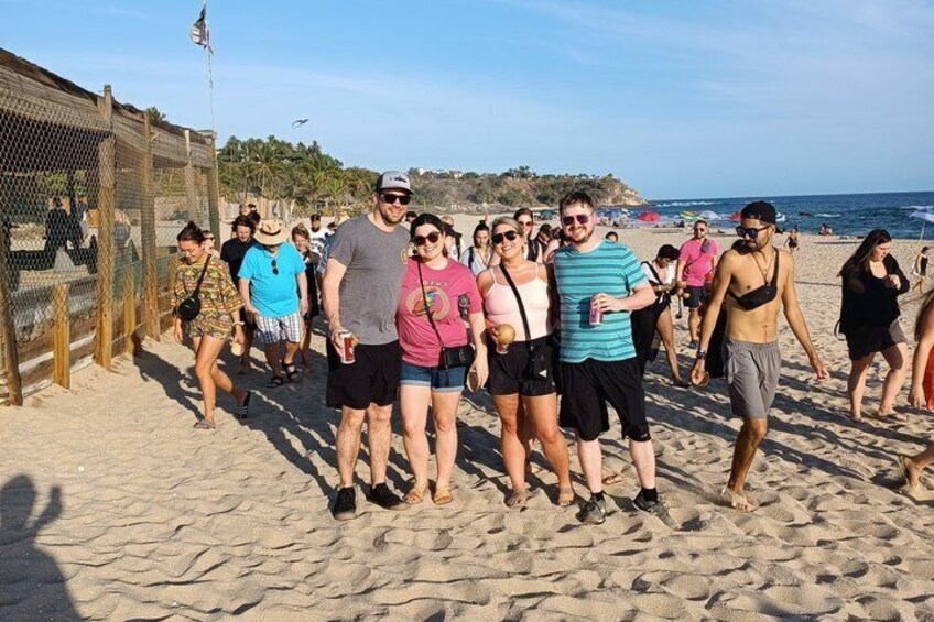 A group of people walking on a sandy beach with a fence and palm trees in the background. 5