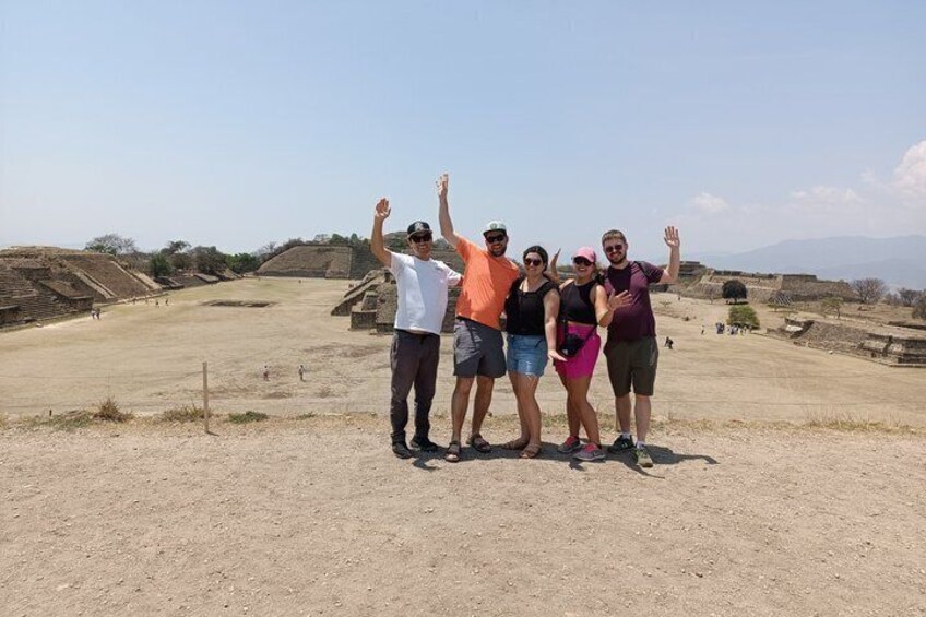 A group of people standing on a dirt field with ruins in the background. 1