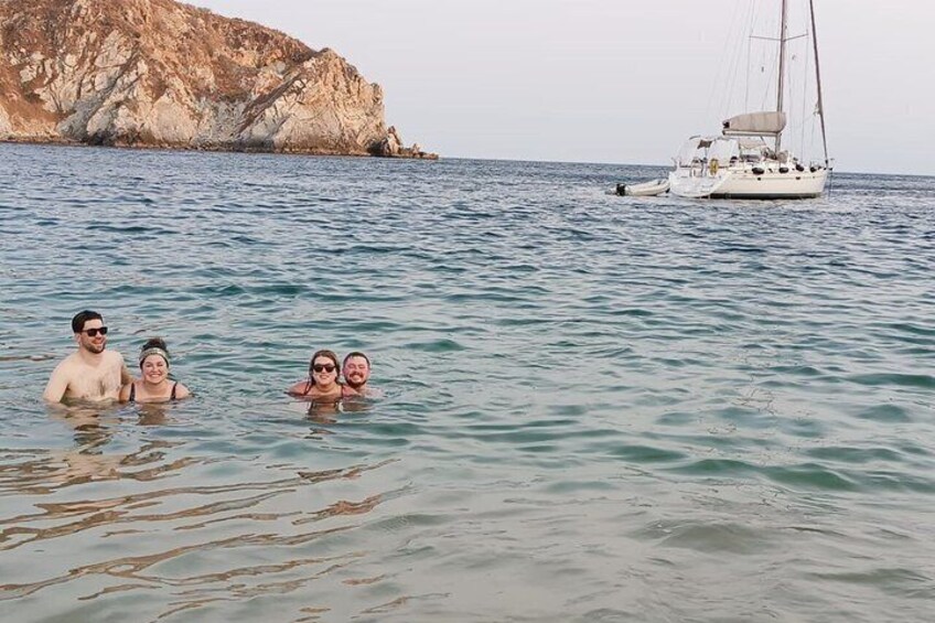 A group of people swimming in calm sea water with a sailboat in the background. 3