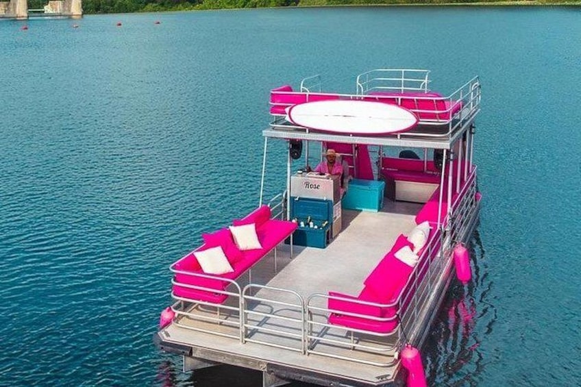 Un bateau rose et blanc, doté d’un pont et d’un espace pour s  ’asseoir, naviguant sur une étendue d’eau. 1