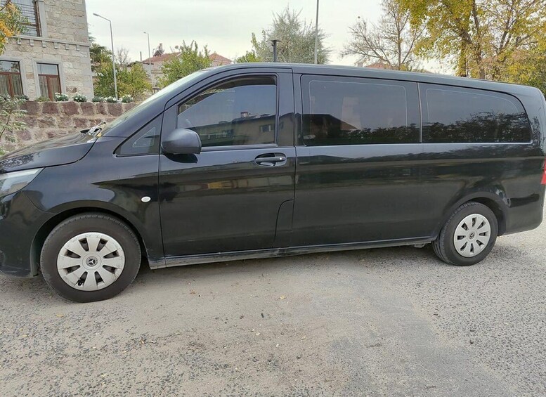 A black van parked on a gravel surface with a stone building and trees in the background. 3