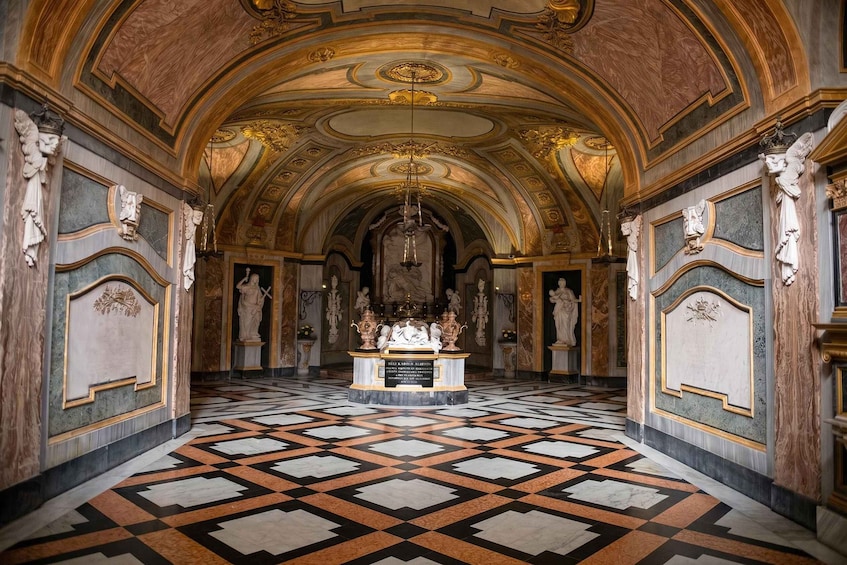 An ornate hallway with a patterned floor, statues, and a central altar. 1