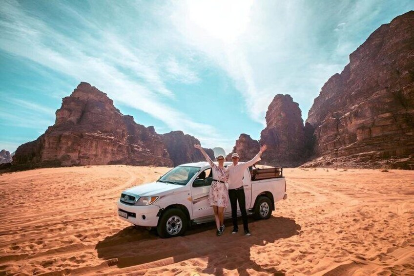 Un pick-up bianco parcheggiato su una sabbiosa distesa desertica, con formazioni rocciose sullo sfondo. 4