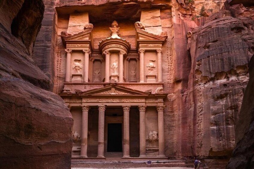 Facciata rocciosa scolpita con colonne e un portale centrale, circondata da formazioni rocciose naturali. 1