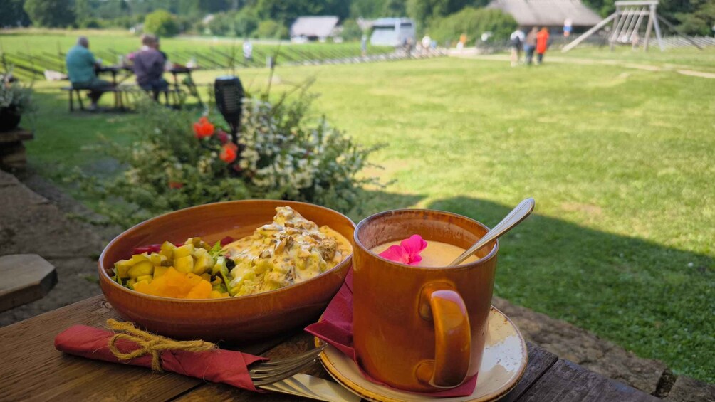 A meal with a bowl of food and a mug on a wooden table outdoors. 5