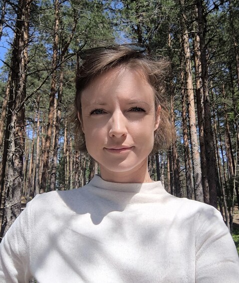 A person in a white sweater standing in a forest with tall trees. 5