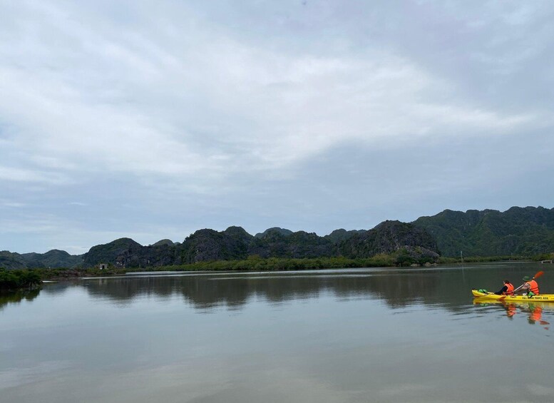 A calm river with kayakers in a yellow kayak, surrounded by lush green hills. 5