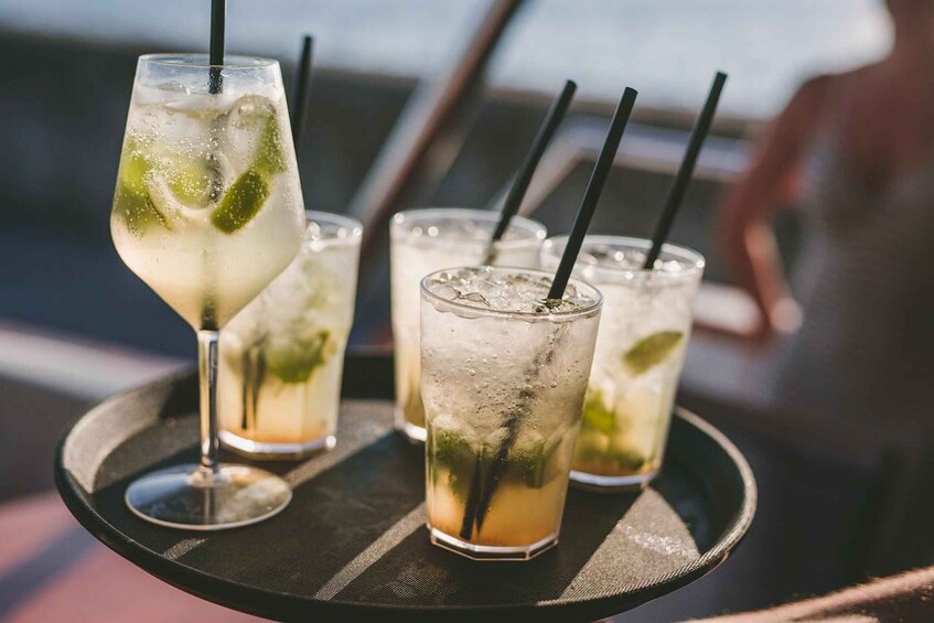 A tray with three glasses of a lime-infused beverage, one with a stemmed glass and two with straight sides, all with black straws. 3