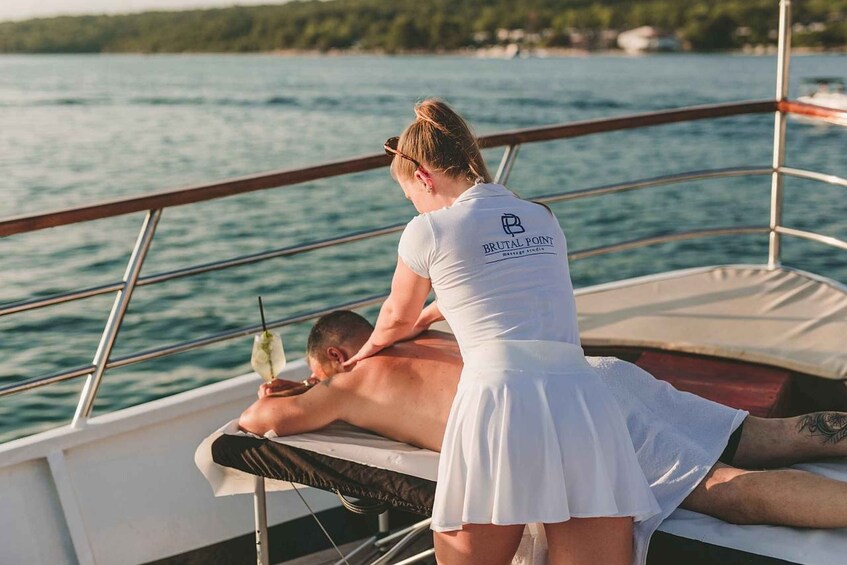 A person receiving a massage on a boat with a 'Brutal Point' logo on their shirt. 4