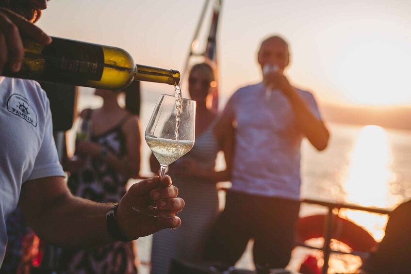 A person pouring wine into a glass on a boat at sunset. 1