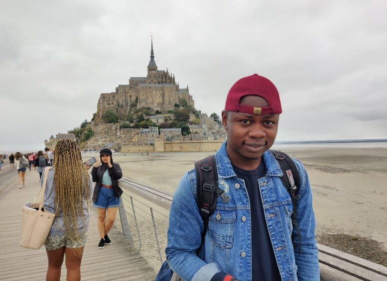 A person in denim jacket and red cap standing on a wooden boardwalk with a historic castle in the background. 2