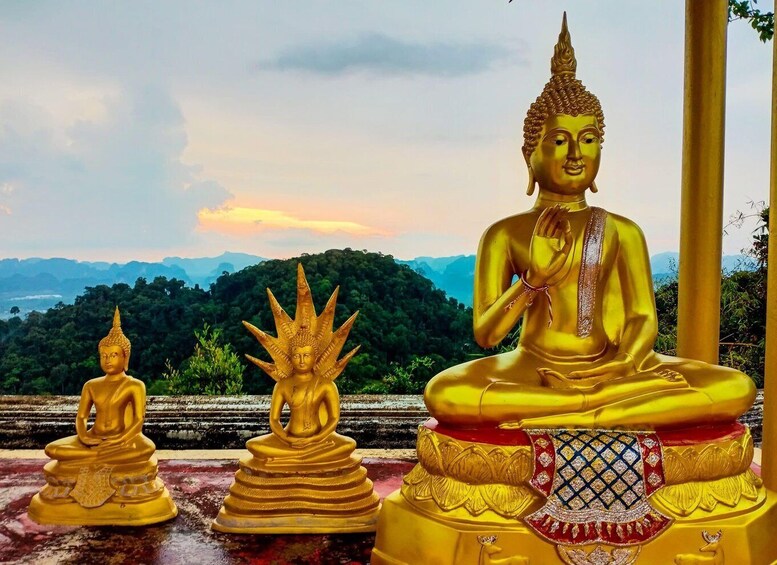 Three golden Buddha statues in a row, set against a backdrop of lush green hills and a clear sky. 1