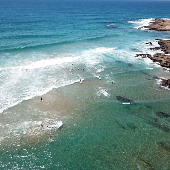 A beach with clear turquoise water, rocky shoreline, and people surfing. 1