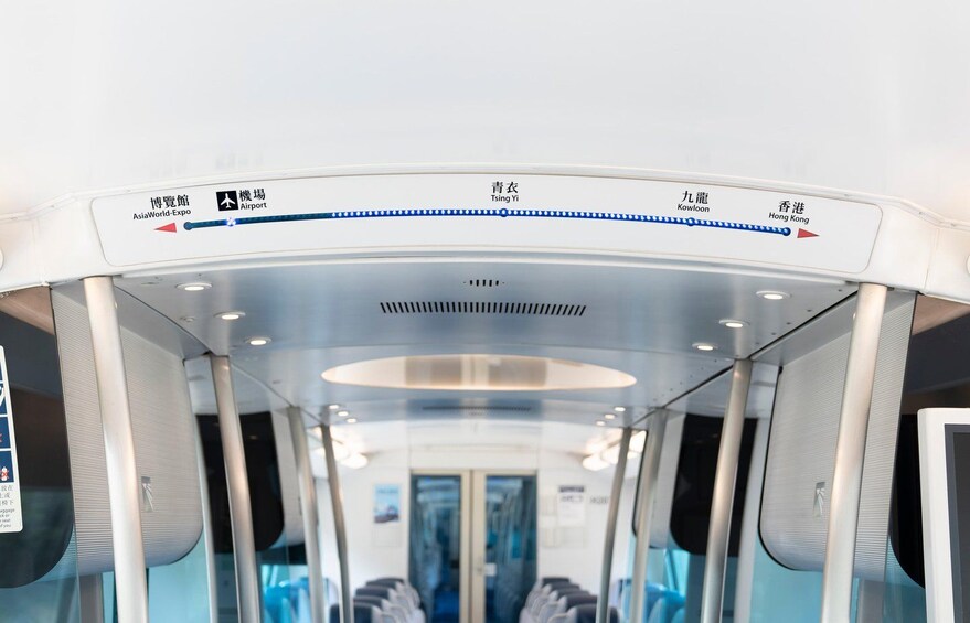A train interior with overhead luggage compartments, a digital display, and seating. 4