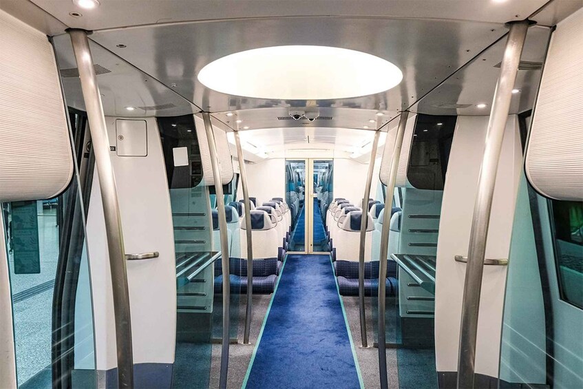 A train interior with a central aisle, overhead lighting, and seating on either side. 4