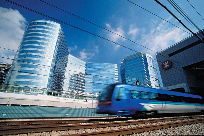 A high-speed train passing by modern glass buildings with a clear blue sky. 1