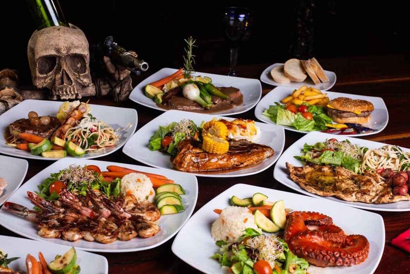 A variety of plated dishes including seafood, vegetables, and meats, arranged on a table with a skull and wine glass in the background. 5