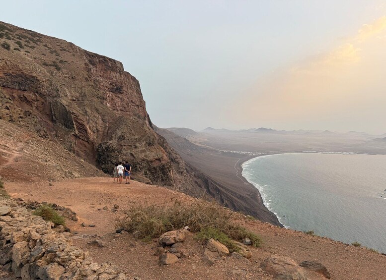 A rocky cliff overlooking a calm sea with a few people standing at the edge. 4