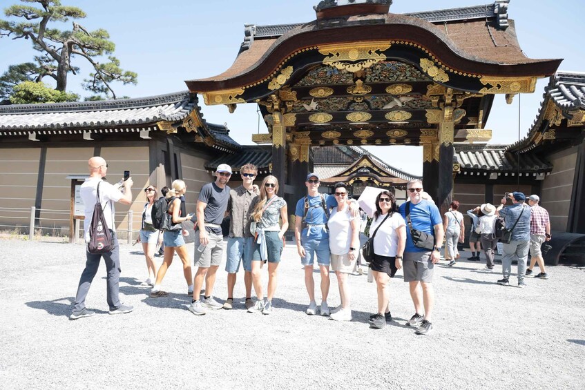 Un grupo de turistas frente a una puerta tradicional japonesa con diseños intrincados y un árbol grande al fondo. 5