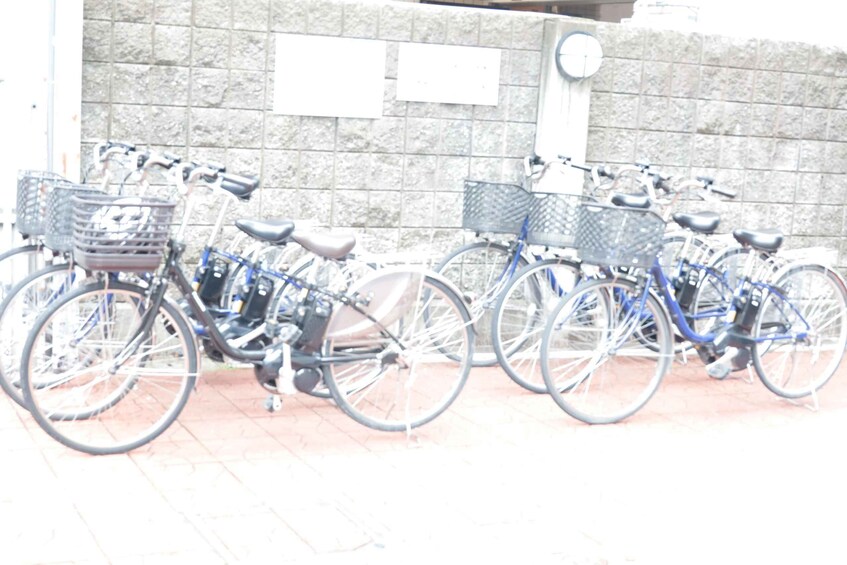 A row of bicycles parked against a stone wall with a clock. 3