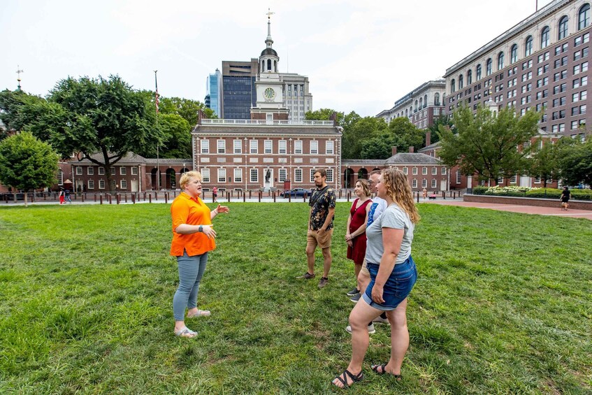 A group of people standing on a grassy field with historic buildings in the background. 1