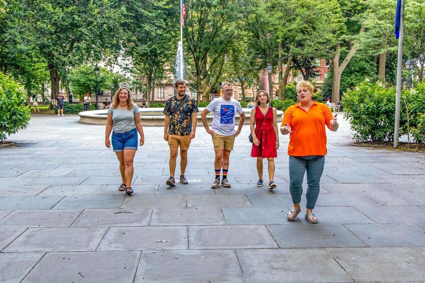 A group of people walking on a paved path in a park with trees and a fountain in the background. 2