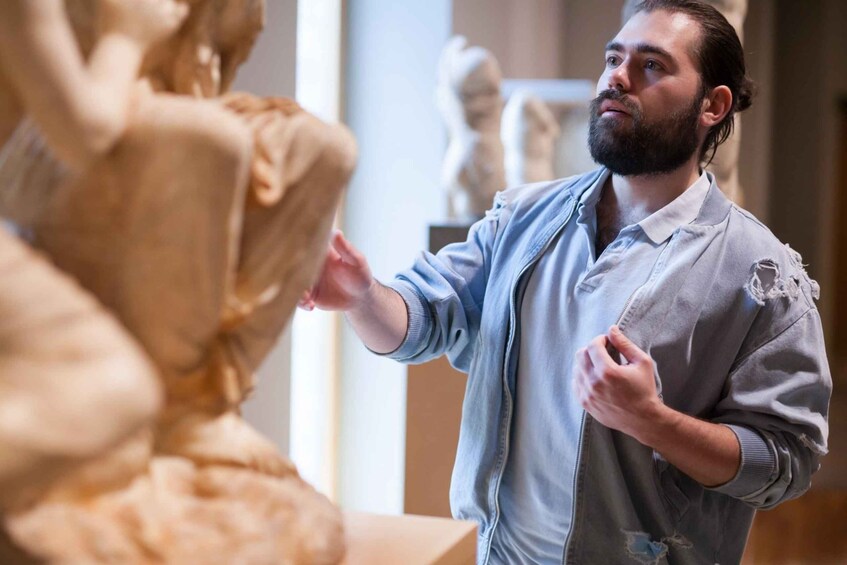 A person in a light blue shirt and grey jacket standing in front of a sculpture. 3