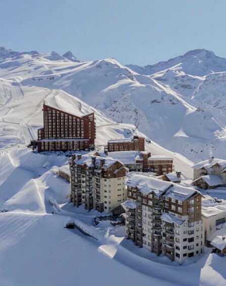 A snow-covered mountain resort with multiple buildings, including a prominent red-brick hotel and several chalet-style structures. 5
