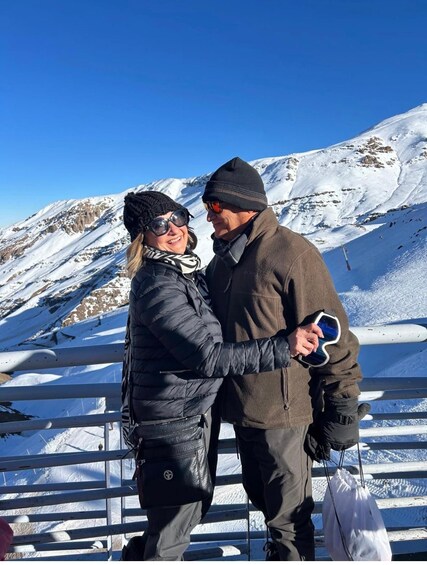 Two people embracing in a snowy mountainous area with a clear blue sky. 2