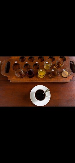 A wooden tray with multiple glasses of different colored liquids and a white cup with a spoon. 5