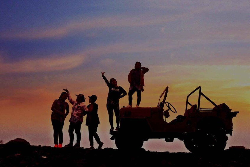 A group of people standing on a vehicle with a sunset in the background. 2