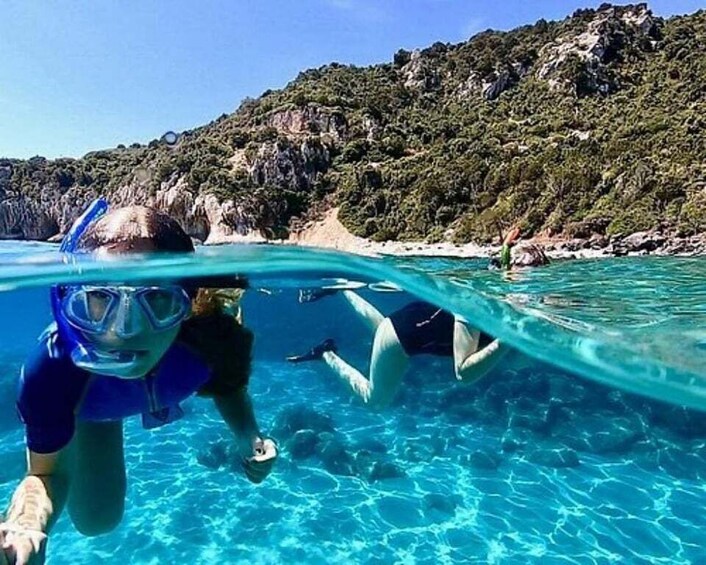 A person snorkeling underwater with clear blue water and a rocky landscape in the background. 1