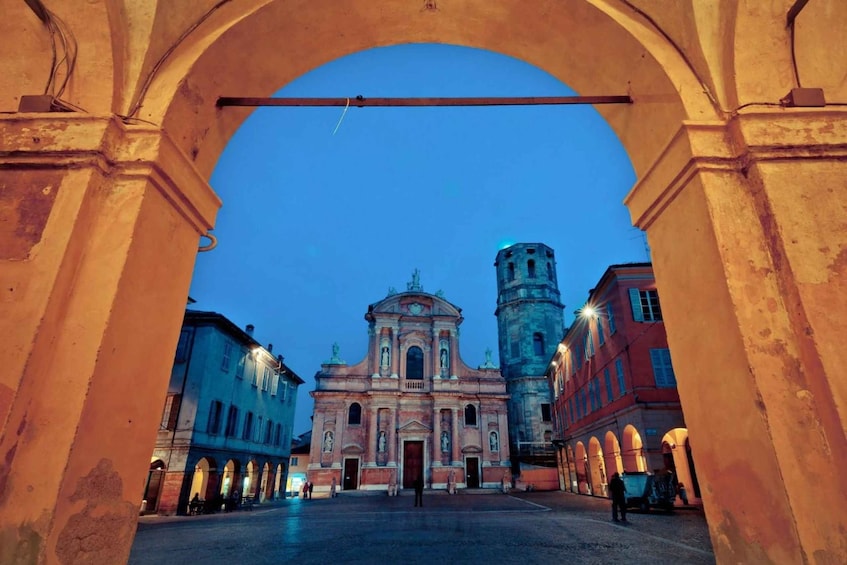 An archway framing a historic building with a bell tower, under twilight sky. 1