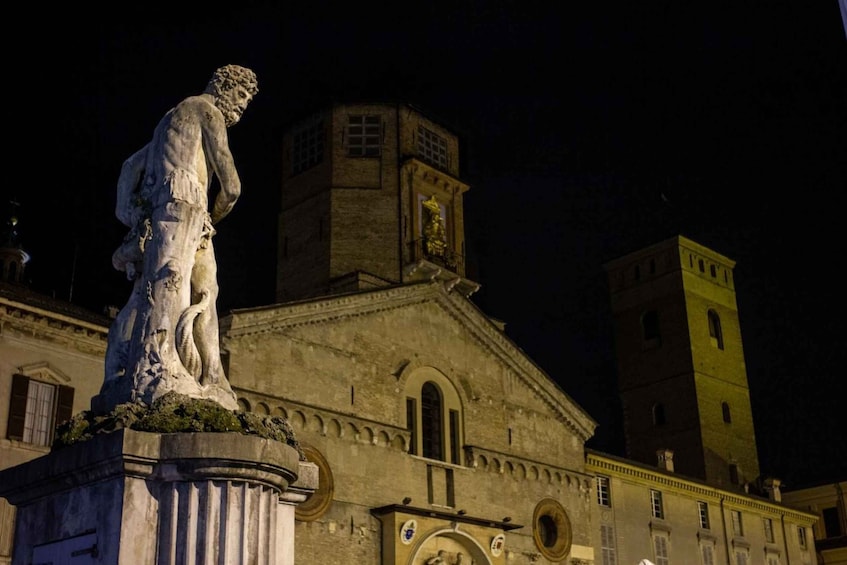 A statue in front of a historic building with a clock tower at night. 5